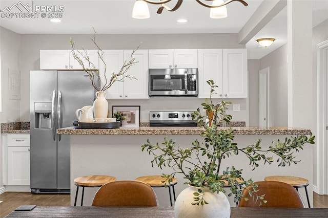 kitchen featuring wood finished floors, recessed lighting, white cabinetry, stone counters, and stainless steel appliances