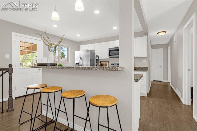 kitchen with appliances with stainless steel finishes, a sink, dark wood finished floors, white cabinetry, and a kitchen bar