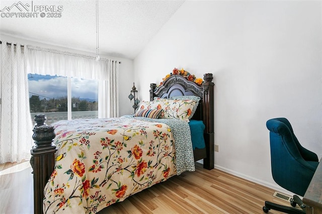 bedroom with baseboards, wood finished floors, visible vents, and vaulted ceiling