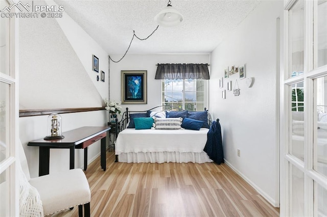 bedroom with a textured ceiling, baseboards, and wood finished floors