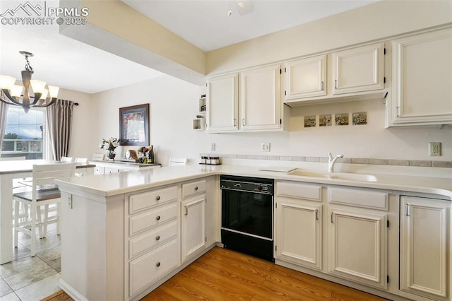 kitchen featuring an inviting chandelier, a sink, dishwasher, light countertops, and a peninsula