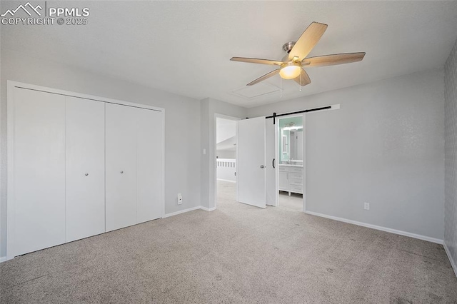 unfurnished bedroom featuring baseboards, a barn door, carpet, and a closet