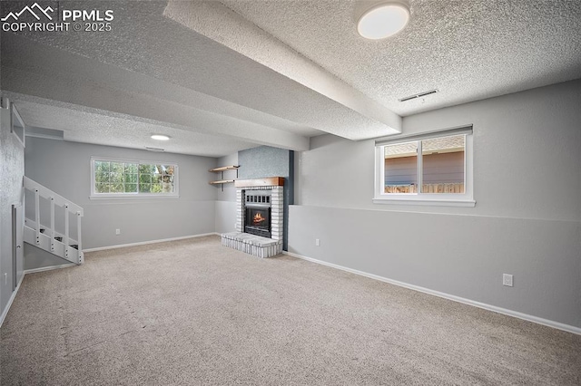 basement featuring visible vents, a brick fireplace, baseboards, a textured ceiling, and carpet flooring