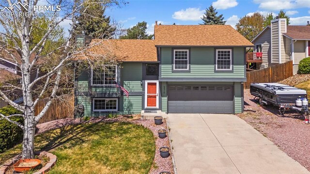 tri-level home featuring a garage, fence, a front yard, a shingled roof, and concrete driveway