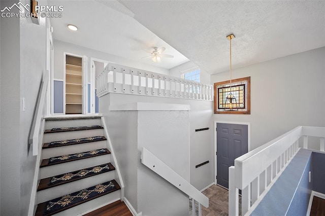 stairway featuring baseboards, a ceiling fan, a textured ceiling, and wood finished floors