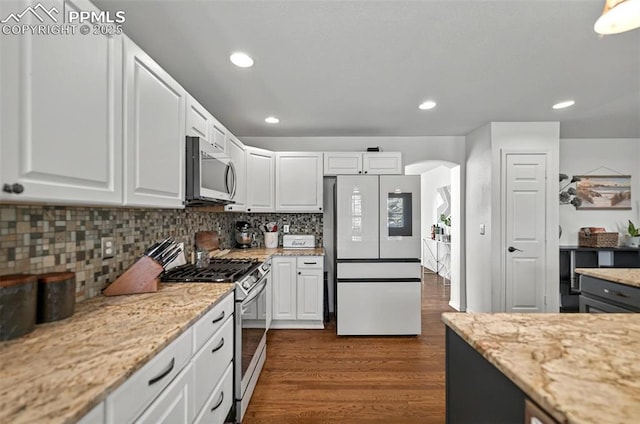 9025 Rochester Dr, Colorado Springs, CO 80920 - kitchen featuring appliances with stainless steel finishes, arched walkways, white cabinets, dark wood-style flooring, and backsplash