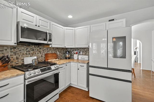 9025 Rochester Dr, Colorado Springs, CO 80920 - kitchen with appliances with stainless steel finishes, arched walkways, wood finished floors, white cabinets, and recessed lighting
