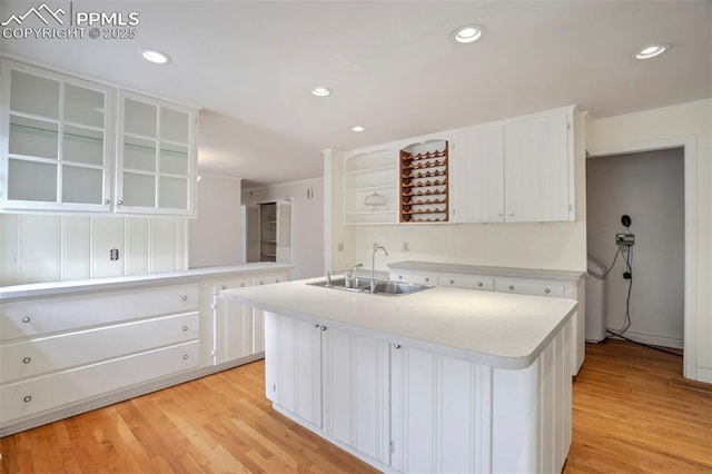 kitchen with open shelves, an island with sink, light countertops, white cabinets, and a sink