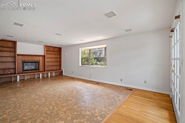 unfurnished living room with baseboards, visible vents, built in shelves, and a fireplace