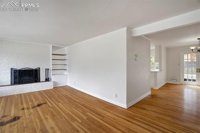 unfurnished living room with crown molding, a brick fireplace, wood finished floors, baseboards, and a chandelier