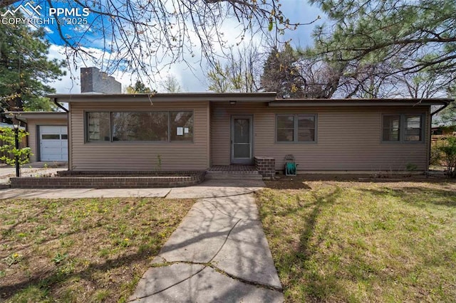 ranch-style home with a chimney, an attached garage, and a front lawn