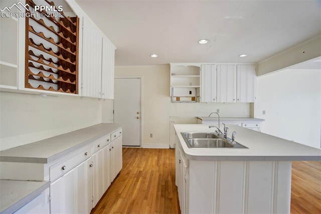 kitchen with open shelves, light wood-type flooring, a sink, light countertops, and white cabinets