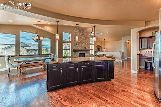 kitchen with freestanding refrigerator, ceiling fan with notable chandelier, wood finished floors, and vaulted ceiling