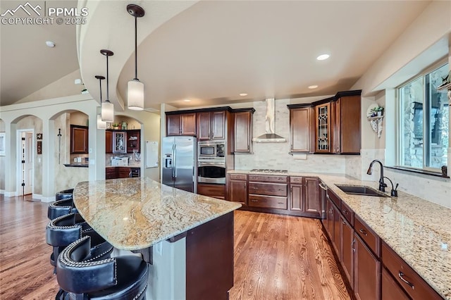 kitchen with a sink, light stone counters, stainless steel appliances, and wall chimney exhaust hood