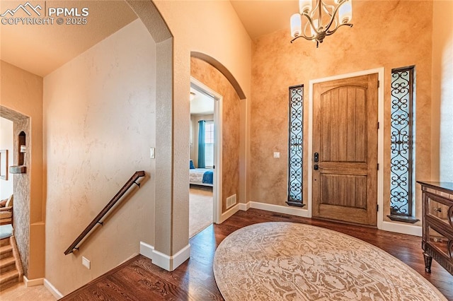 entryway with an inviting chandelier, visible vents, wood finished floors, baseboards, and arched walkways