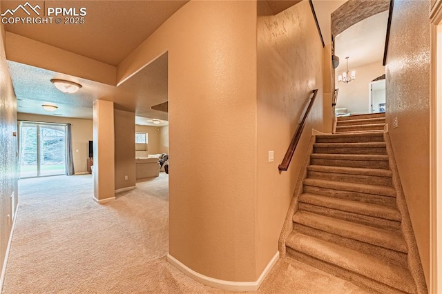 staircase featuring carpet floors, baseboards, a textured wall, and a notable chandelier