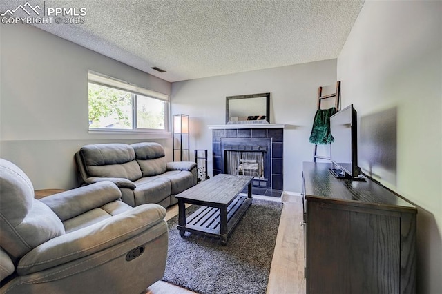 living room with a textured ceiling, a tiled fireplace, wood finished floors, and visible vents