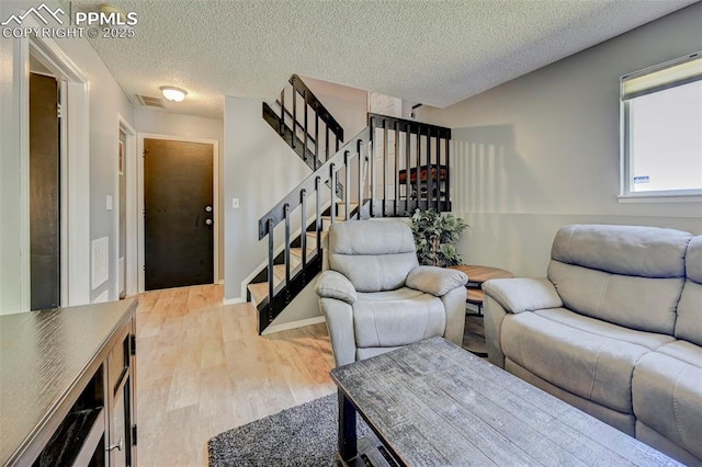 living area featuring stairway, a textured ceiling, light wood-type flooring, and visible vents