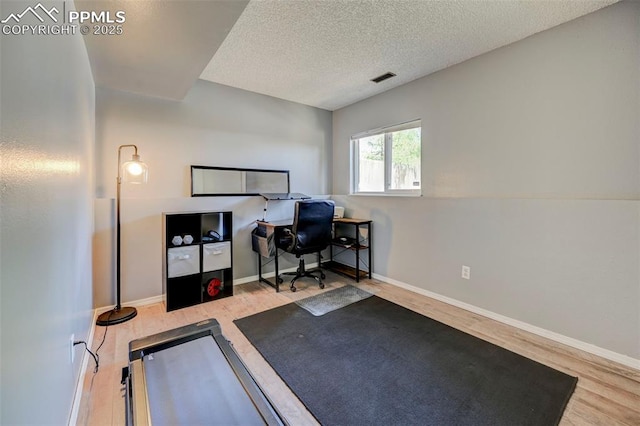exercise room with a textured ceiling, visible vents, wood finished floors, and baseboards