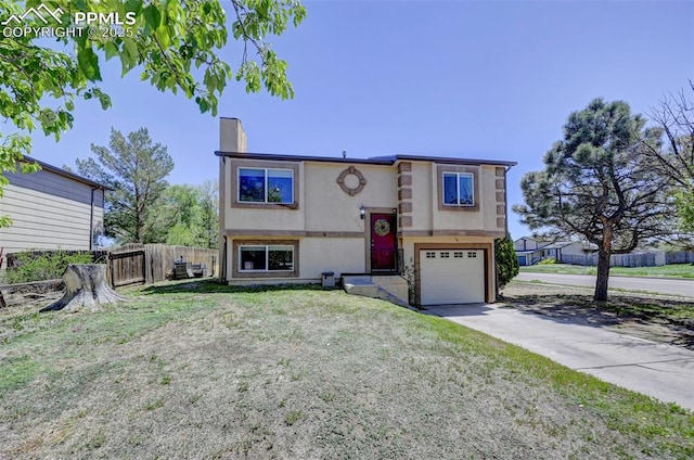 split foyer home with a garage, stucco siding, a chimney, fence, and concrete driveway