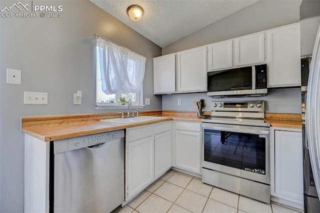 kitchen featuring light tile patterned floors, a sink, a textured ceiling, appliances with stainless steel finishes, and lofted ceiling