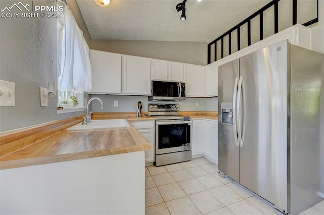 kitchen featuring a sink, a textured ceiling, appliances with stainless steel finishes, vaulted ceiling, and light tile patterned flooring