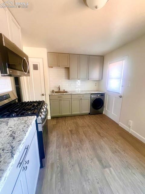 1229 E Caramillo St, Colorado Springs, CO 80909 - kitchen with washer / dryer, stainless steel appliances, a sink, decorative backsplash, and wood finished floors