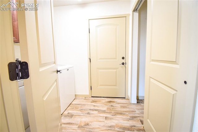 hall with light wood-style floors, baseboards, and washer and dryer