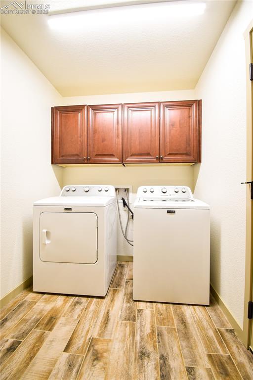 clothes washing area featuring baseboards, light wood-style flooring, and cabinet space
