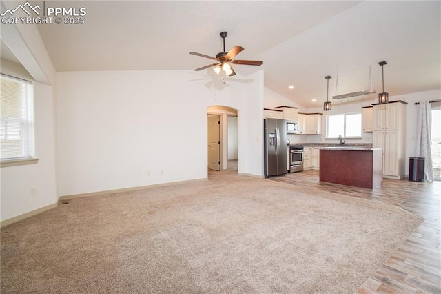 unfurnished living room featuring a sink, lofted ceiling, baseboards, ceiling fan, and arched walkways