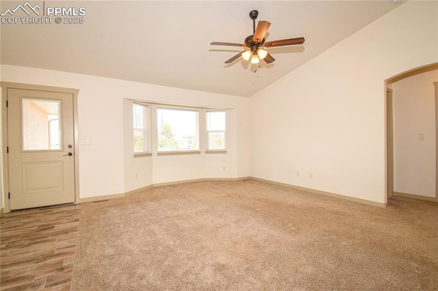 interior space with a ceiling fan, arched walkways, vaulted ceiling, baseboards, and light carpet