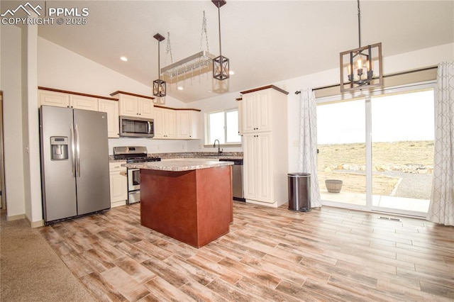 kitchen with an inviting chandelier, light wood-style flooring, stainless steel appliances, lofted ceiling, and a kitchen island