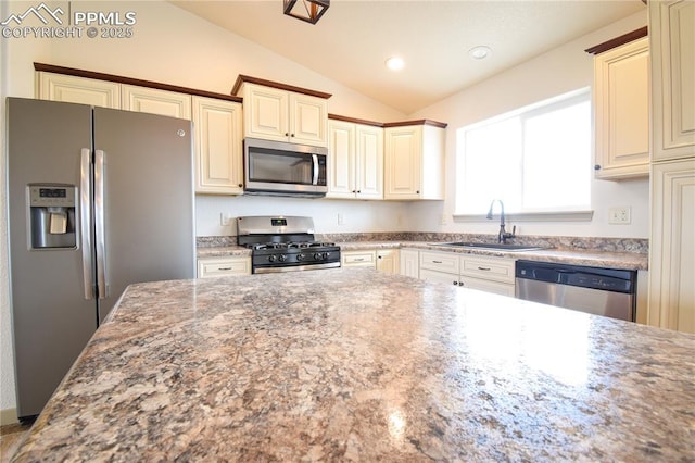 kitchen featuring lofted ceiling, stone countertops, cream cabinets, a sink, and stainless steel appliances