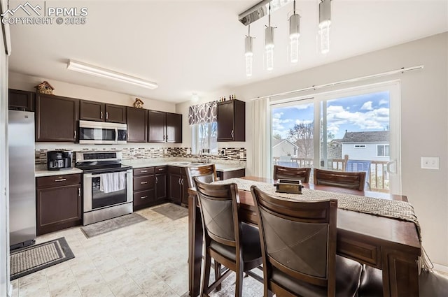 kitchen with dark brown cabinets, appliances with stainless steel finishes, light countertops, light floors, and pendant lighting