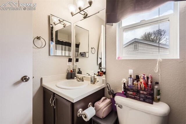 bathroom with toilet, a textured wall, and vanity