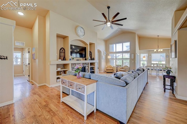 living room with visible vents, a stone fireplace, light wood-style flooring, and ceiling fan with notable chandelier