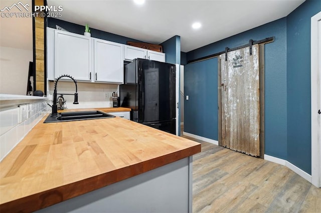 kitchen with freestanding refrigerator, butcher block counters, tasteful backsplash, a sink, and light wood finished floors