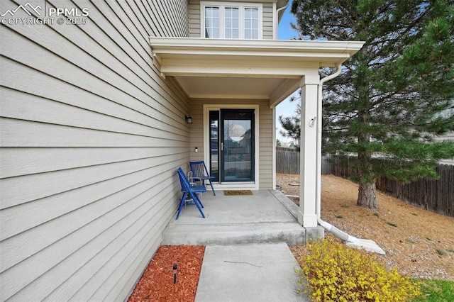 view of exterior entry featuring fence and a porch