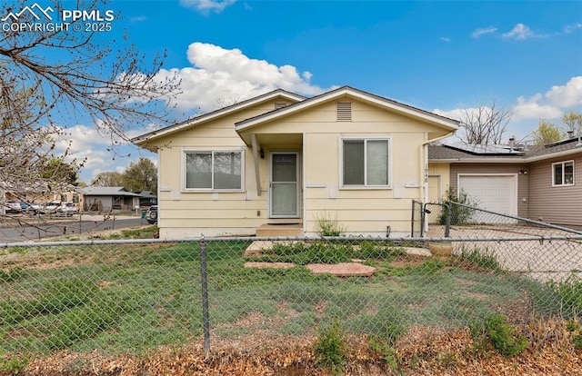 bungalow with an attached garage, a fenced front yard, a front yard, solar panels, and driveway