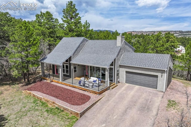 ranch-style house with roof with shingles, a garage, a porch, a chimney, and driveway