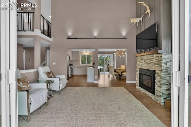 living area featuring a stone fireplace, wood finished floors, a chandelier, a high ceiling, and stairs