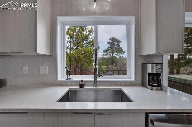 kitchen with stainless steel dishwasher, a sink, backsplash, and light stone counters