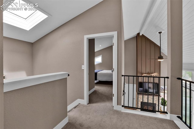 hall featuring carpet floors, baseboards, lofted ceiling with skylight, and an upstairs landing
