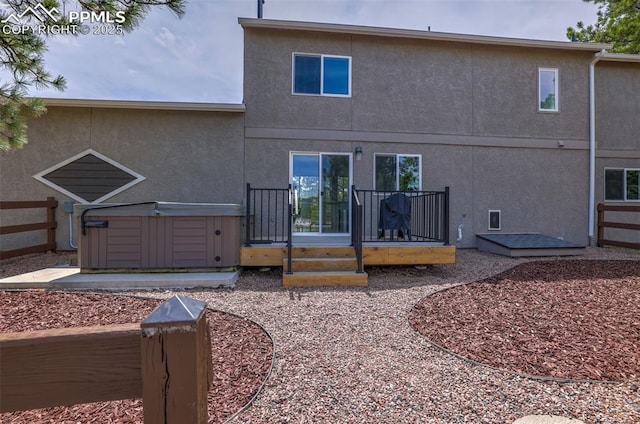 rear view of house with stucco siding, a hot tub, and a deck