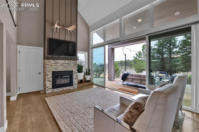 living room featuring high vaulted ceiling, a stone fireplace, baseboards, and light wood-style floors