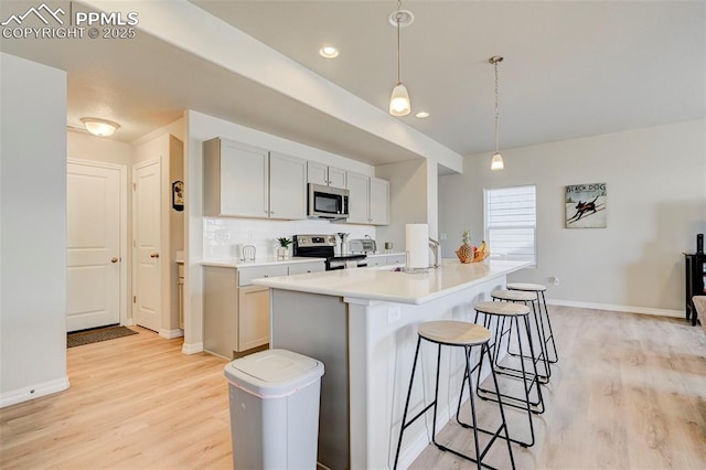 kitchen featuring a breakfast bar, light countertops, a sink, light wood finished floors, and appliances with stainless steel finishes