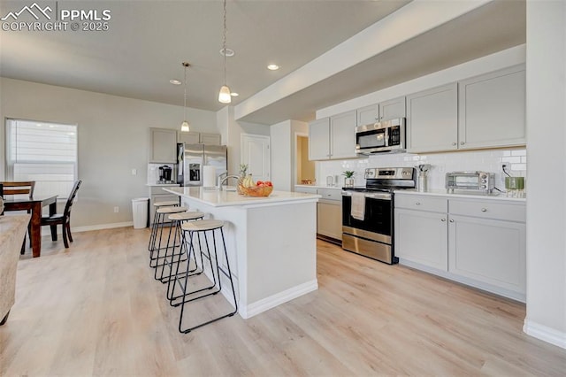 kitchen featuring appliances with stainless steel finishes, light wood finished floors, light countertops, a kitchen bar, and backsplash