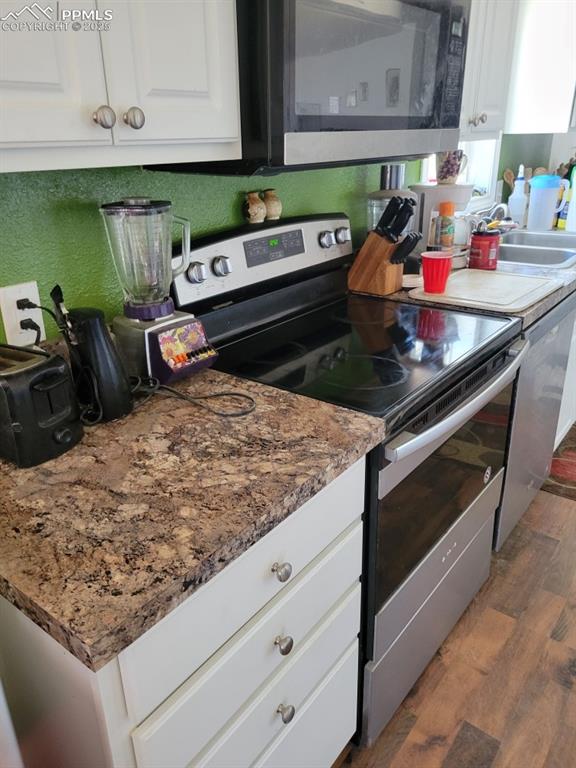 823 7th St, Hugo, CO 80821 - kitchen featuring appliances with stainless steel finishes, wood finished floors, white cabinets, and light stone counters