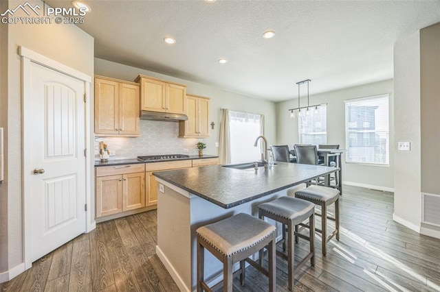 kitchen featuring light brown cabinets, a sink, dark countertops, a breakfast bar, and dark wood-style flooring