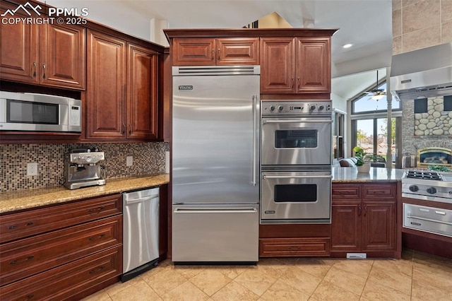 kitchen with ceiling fan, a stone fireplace, tasteful backsplash, light stone countertops, and stainless steel appliances